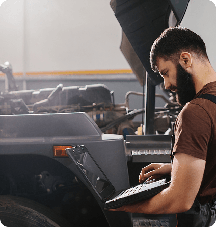 A man working on a vehicle with a laptop in hand.